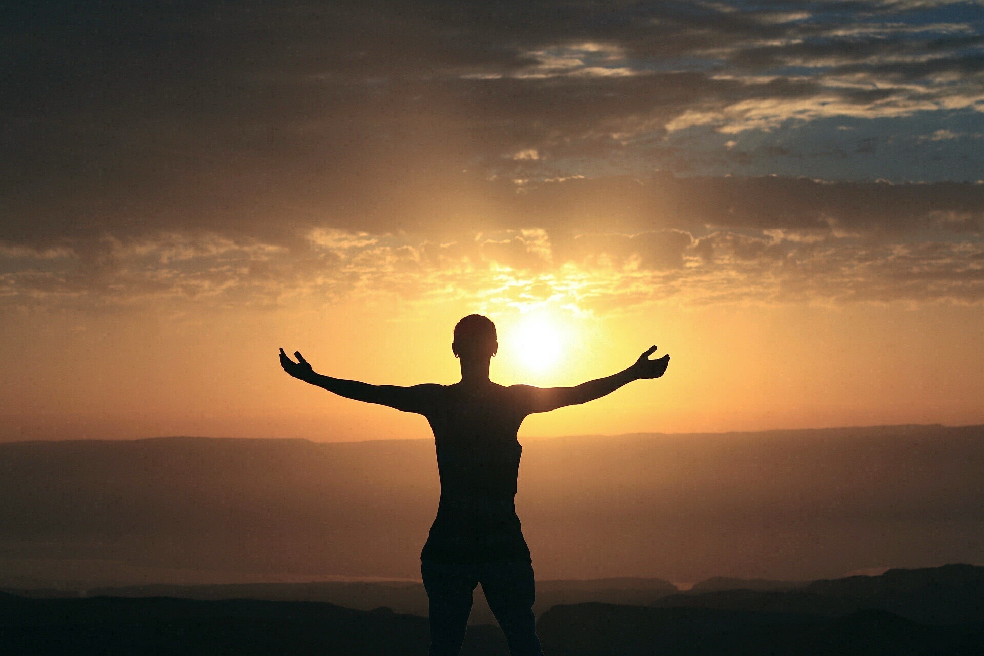 Femme bras ouverts face à un coucher de soleil symbolisant l’épanouissement et la découverte de sa mission de vie